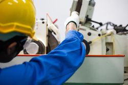 Male in blue jumpsuit and PPE gear operating controller in industrial work space