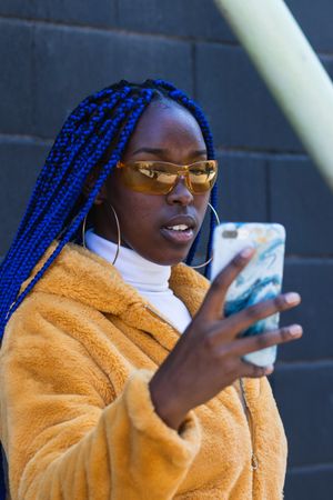 woman in trendy outfit browsing cellphone in city