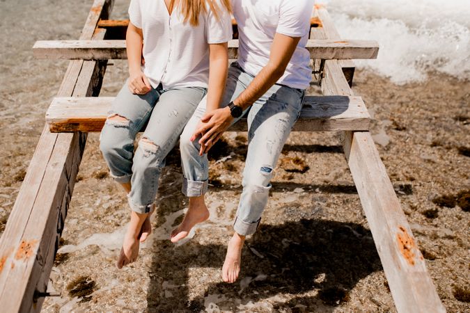 Glad lovers sitting on destroyed pier on seashore