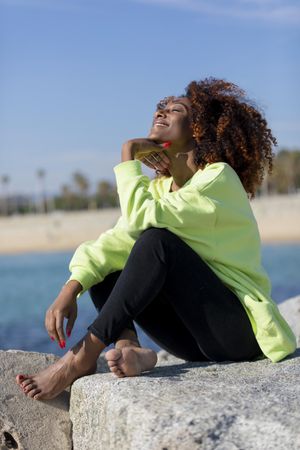 Happy female in green shirt sitting on rocks near coast