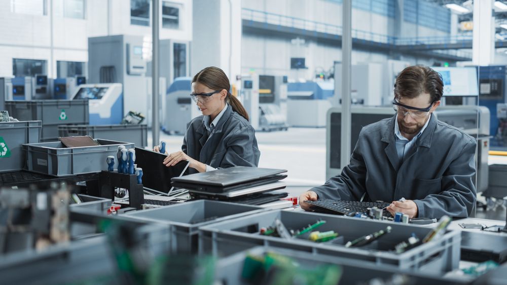 Male And Female Employees Taking Apart Old Laptops To Recycle Electronic Components For Sustainable Devices Production At Electronics Factory.