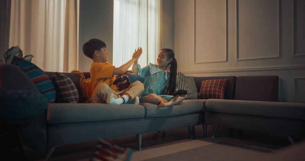 Cute Little Siblings Playing Video Game On Gaming Station On The Sofa In Cozy Living Room.