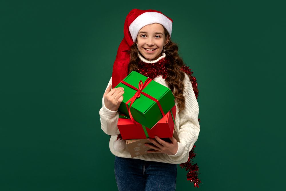 Smiling girl in Santa hat holding Christmas presents.