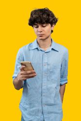 Young man using a smartphone on a vibrant yellow background.
