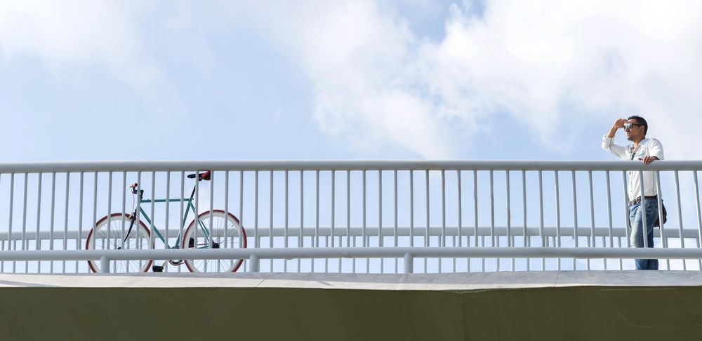 Looking up at male on bridge with bike looking into the distance