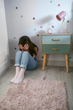 Unrecognizable little girl covering her face with hands sitting on the floor