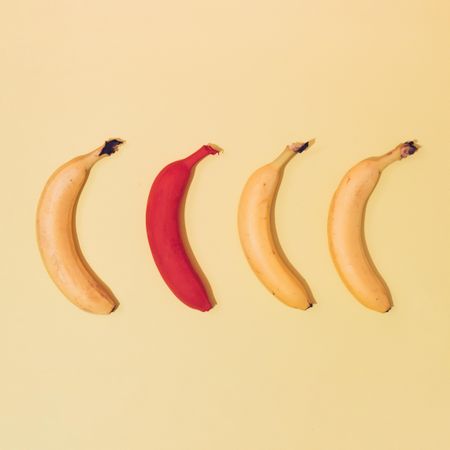 Four bananas against yellow background, one painted in red