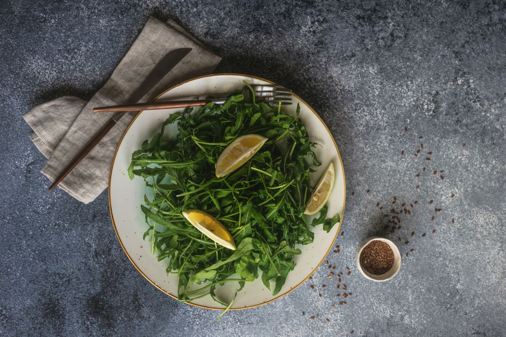 Top view of healthy vegetable salad with organic arugula, lemon and flax seeds on stone background