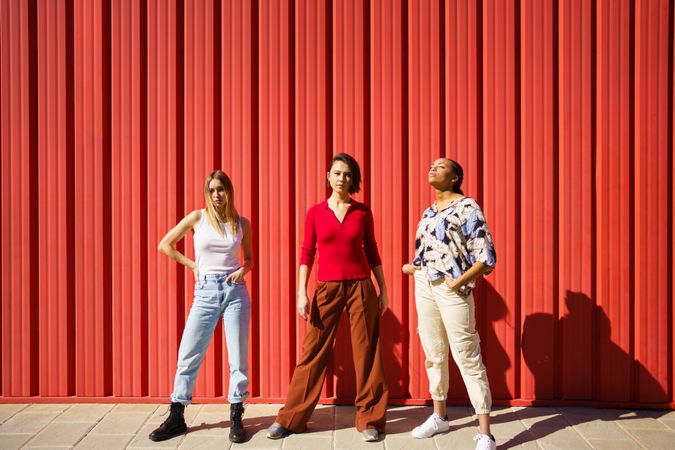 Three proud women posing in front of red wall on sunny day