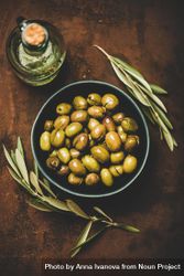Bowl of olives on wooden table with garnish and bottle of olive oil 48MoZb