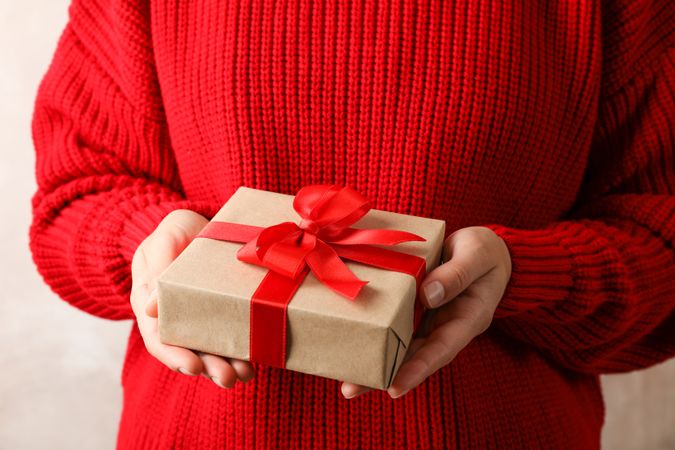 Woman in red sweater holding present with bow, space for text