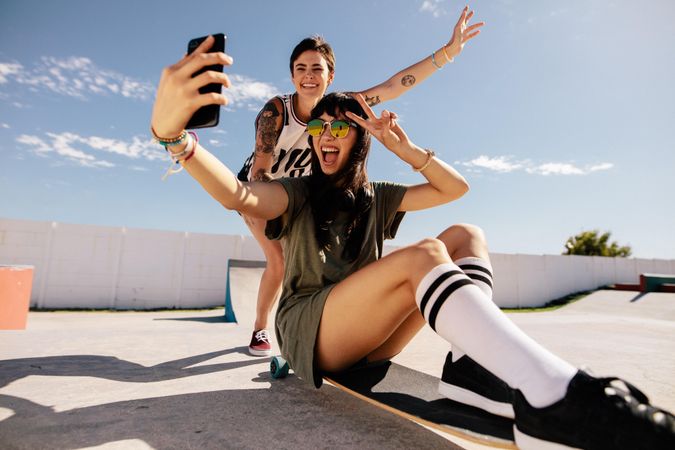 Woman riding on skateboard taking selfie with friends pushing from behind