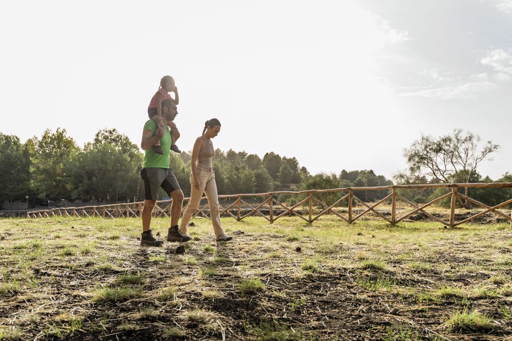 Father carrying daughter on shoulders while walking with mom on countryside path