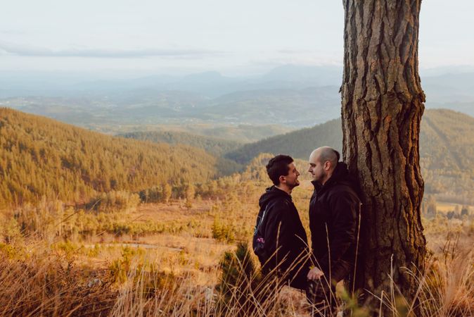 Smiling men hugging near tree in forest on hill