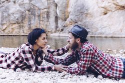 Positive woman and man resting on stone shore near river