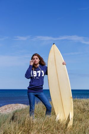 Woman with surfboard in seaside with dry vegetation