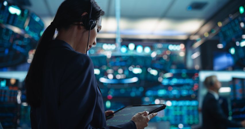 Young Asian Female Broker Working on Tablet Computer on Stock Exchange Floor.