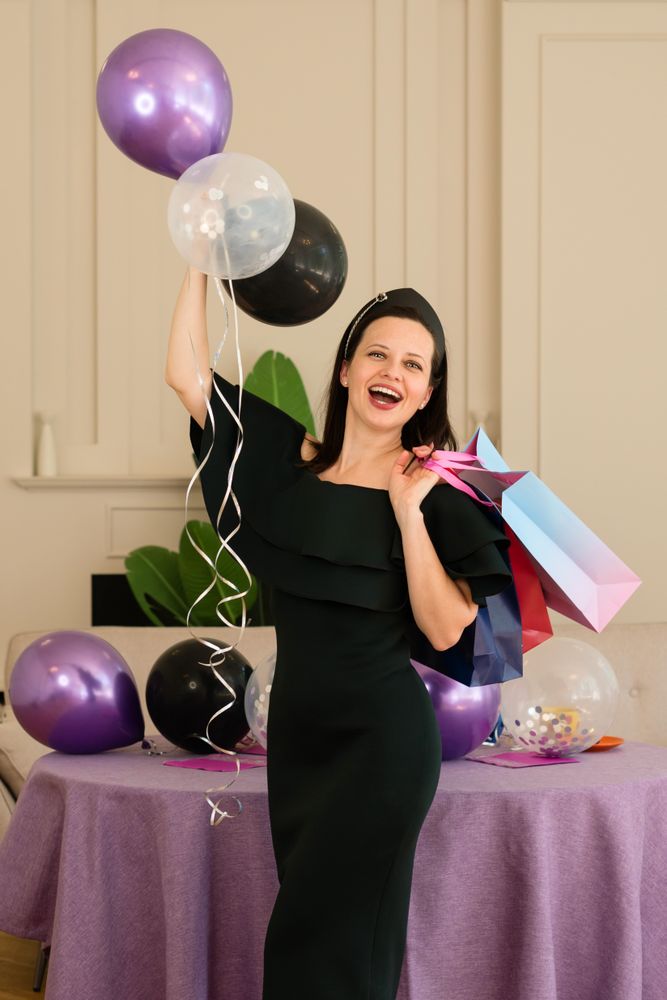 Woman joyfully posing with balloons and gift bags.
