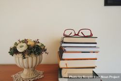 Flower vase beside stack of books with eyeglasses on top 0LXBD0