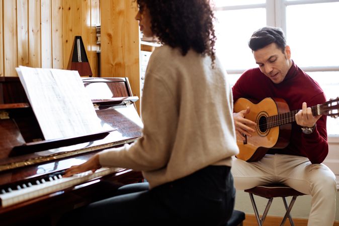 Woman playing piano near man playing guitar in studio