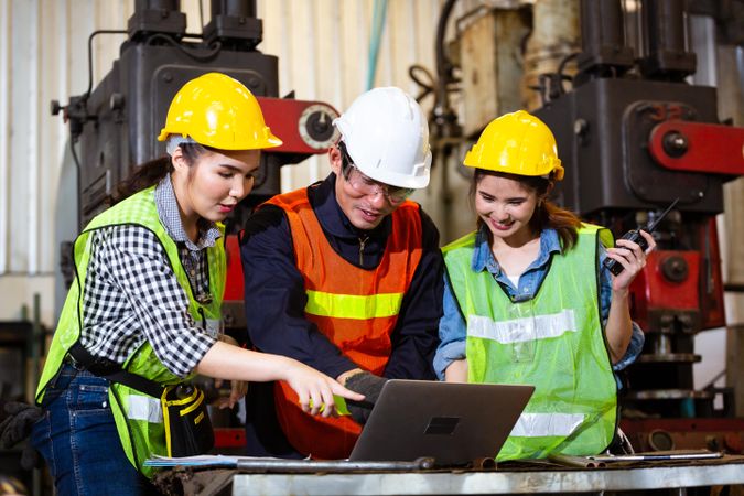 Man and two women discussing plans on laptop in industrial plant