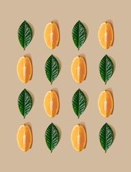 Pattern of green leaves and orange slices on  pastel sand background
