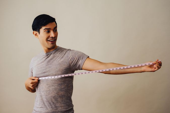 Smiling Hispanic male holding out measuring tape in beige studio shoot