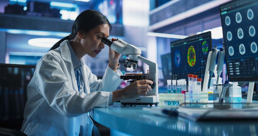 Medical Research And Development Center: Female Asian Scientist Using Microscope To Analyze Petri Dish Sample.