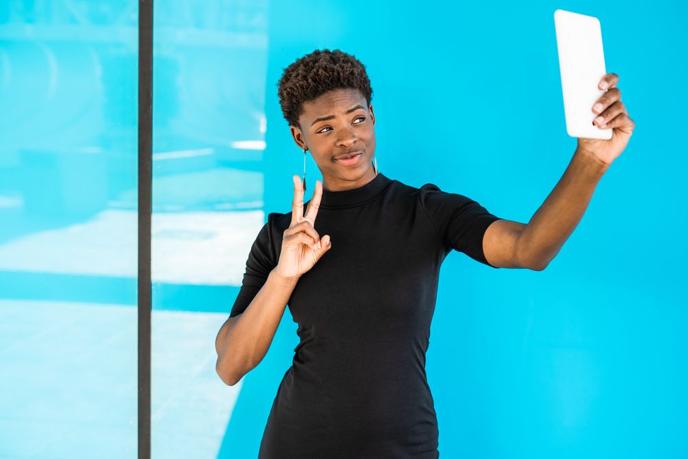 Content female taking selfie and gesturing peace sign