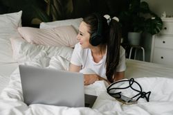 Woman in headphones using laptop on bed