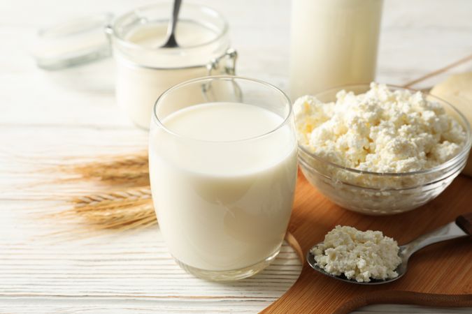Spikelets of wheat, dairy products and board on wood background, copy space