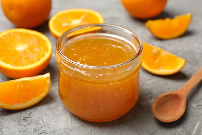 Oranges, spoon and glass jar with jam on gray background, close up