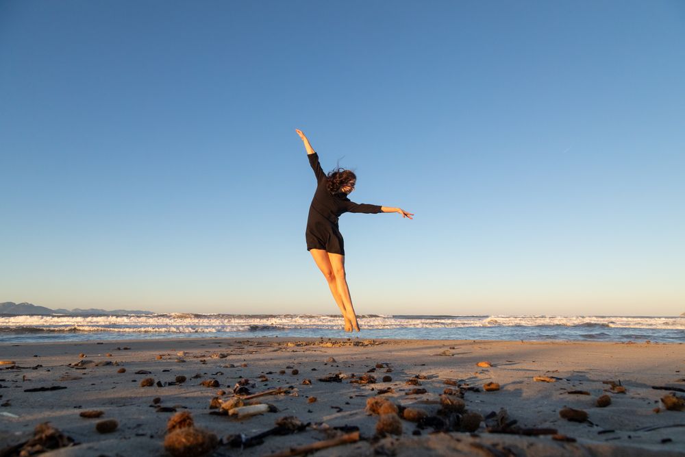 Young woman dancing and posing near water on shore