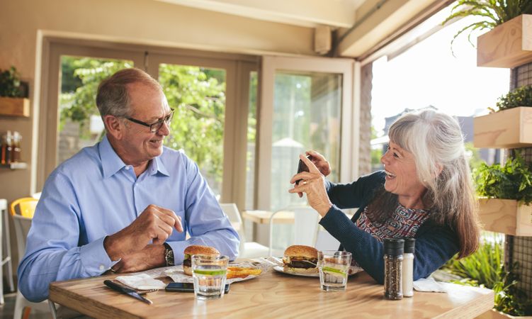 Smiling older woman taking picture of her husband at a restaurant