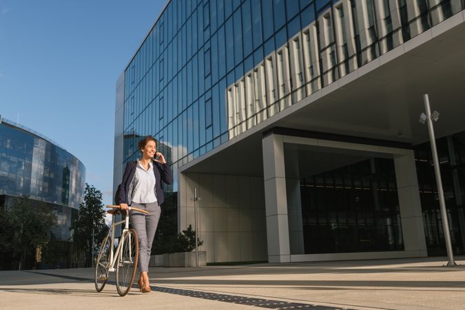 Cheerful manager with bicycle talking on smartphone