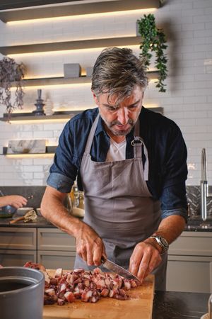 Mature man cutting meat in kitchen