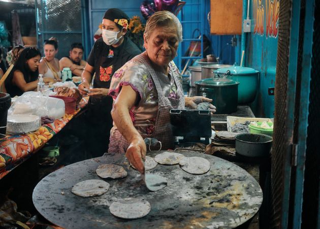 Woman putting fresh tortillas on outdoor grill
