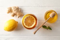 Glass of tea with lemon, mint, honey, dipper and ginger on wooden background, top view