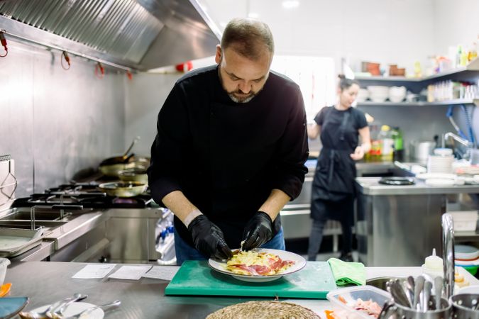Male chef in gloves dressing assorted food in kitchen