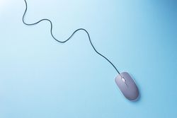 Computer mouse with cable attached laying diagonally on light blue background in