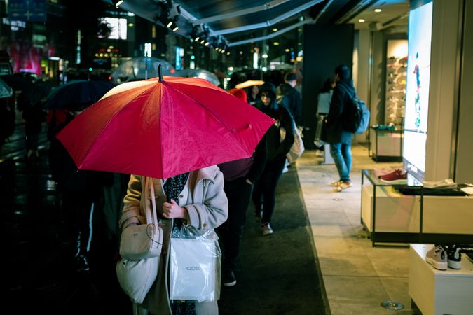 Person holding red umbrella and walking on sidewalk during night time