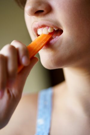 Crop anonymous girl biting into healthy carrot stick