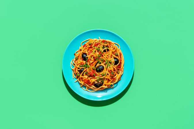 Spaghetti puttanesca plate, above view on a green background