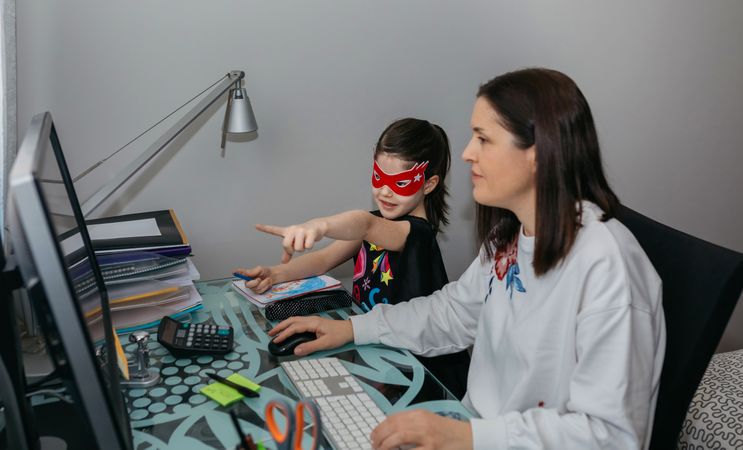 Woman teleworking with daughter showing her a drawing