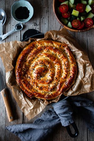From above crop cook holding hot baking dish with fresh puff pastry and serving piece of borek on plateFaceless person serving homemade borek on wooden table