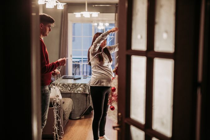 Young couple expecting baby arranging Christmas tree at home