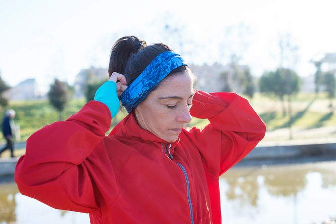 Side view of female adjusting ear warmers outdoors in the grass on sunny fall day