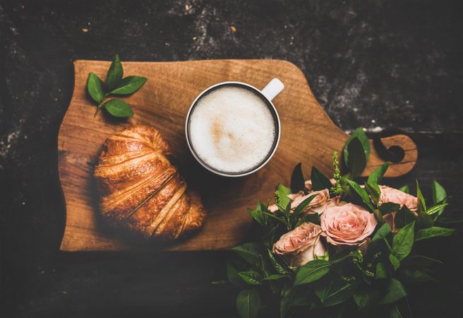 Coffee with croissants and pink roses on wooden board