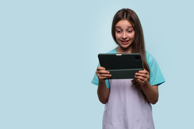 Young girl looking surprised while reading something on tablet.
