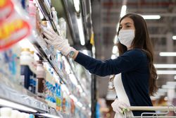 Woman in mask and gloves reaching for milk in dairy aisle